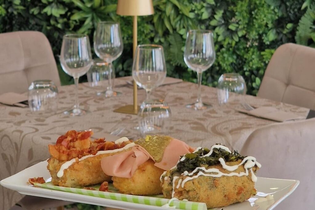 Arancini con maionese e mortadella, tavola apparecchiata sullo sfondo