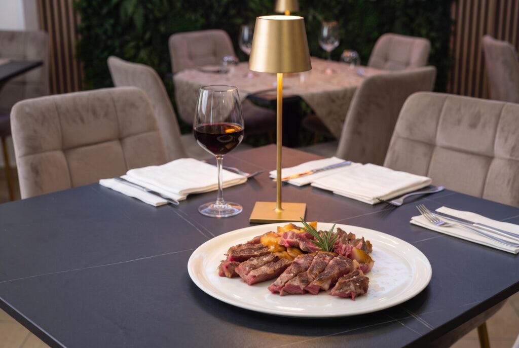 Tagliata di manzo al sangue con rosmarino e sale grosso su piatto bianco, con un calice di vino rosso