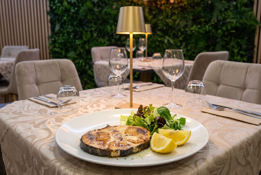 Trancia di pesce alla griglia con limone e insalata su piatto bianco, tavolo apparecchiato