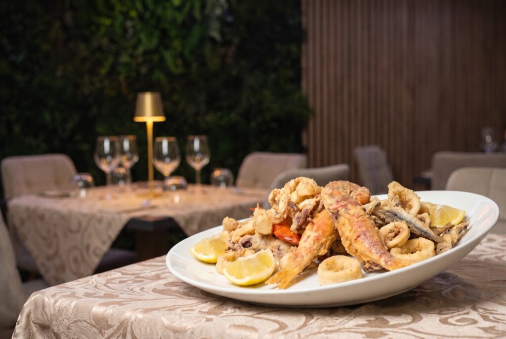 Piatto ovale di frittura mista di pesce con limoni su tavola con tovaglia champagne