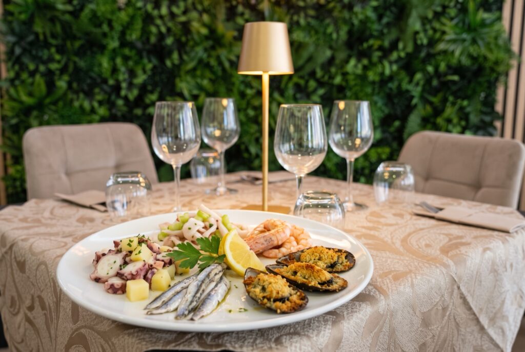 Antipasto misto di mare: polpo, alici marinate, gamberi e cozze gratinate su piatto bianco