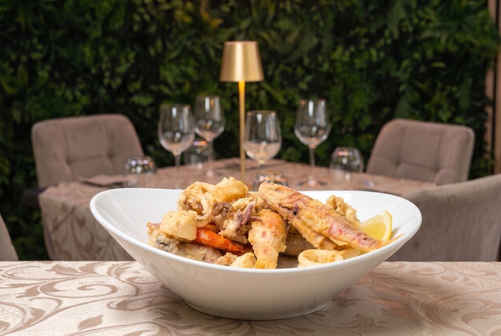 Frittura mista di pesce: calamari, triglie, gamberi e alici su piatto bianco con limone