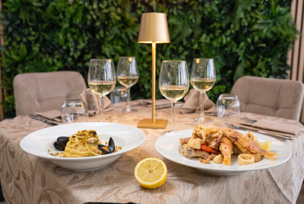 Tavola apparecchiata con spaghetti alle cozze e frittura di pesce, calici di vino bianco