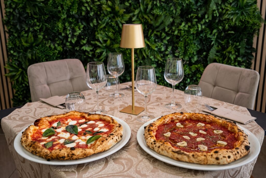 Pizza Margherita e pizza Marinara su piatti bianchi, tavolo apparecchiato con tovaglia damascata e parete verde