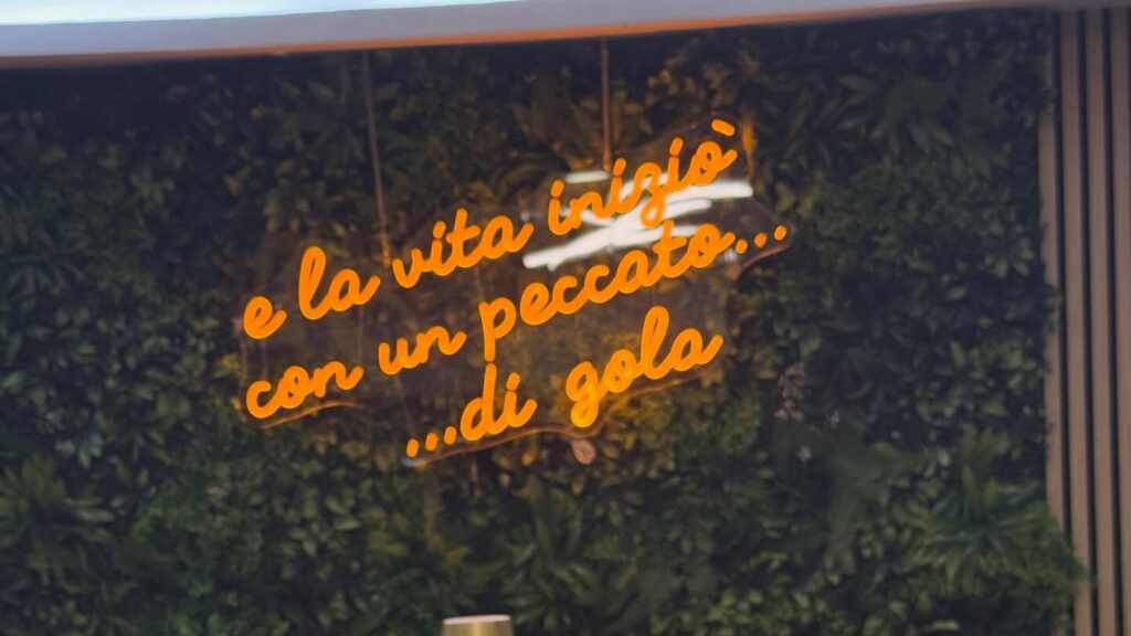 Parete verde con insegna al neon: e la vita inizia con un peccato di gola