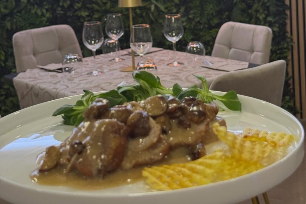 Secondo piatto con funghi e patatine a waffle, tavola apparecchiata sullo sfondo
