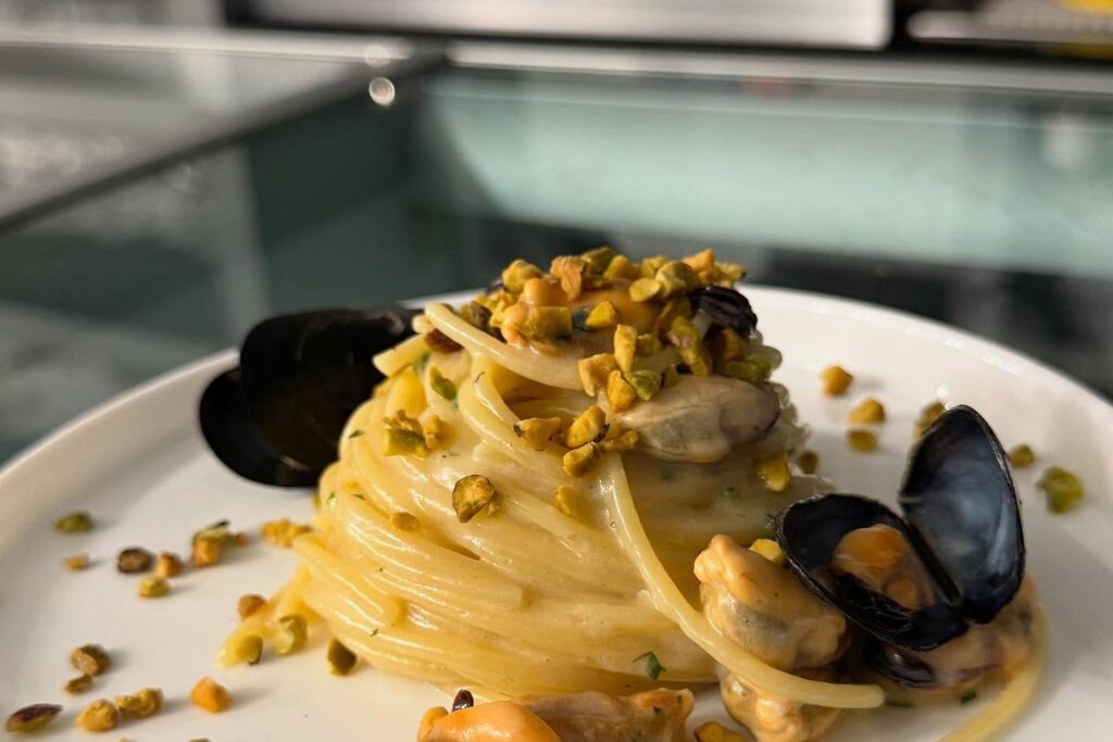 Spaghetti con cozze e granella di pistacchio in piatto bianco