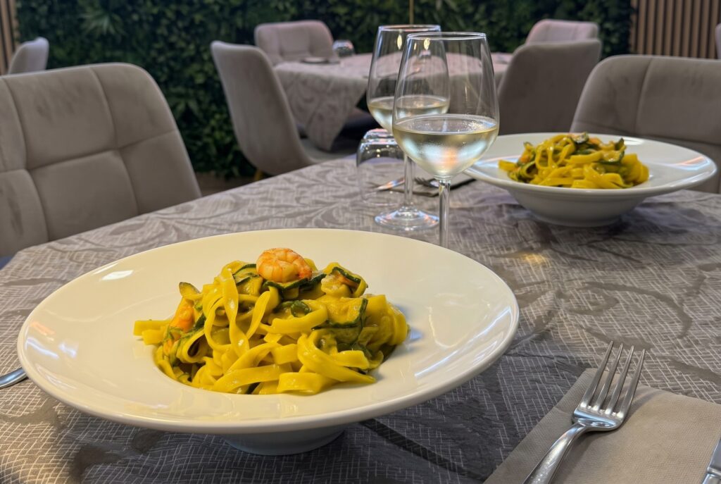 Due piatti di tagliatelle con gamberi, zucchine e zafferano sul tavolo con due calici di vino bianco