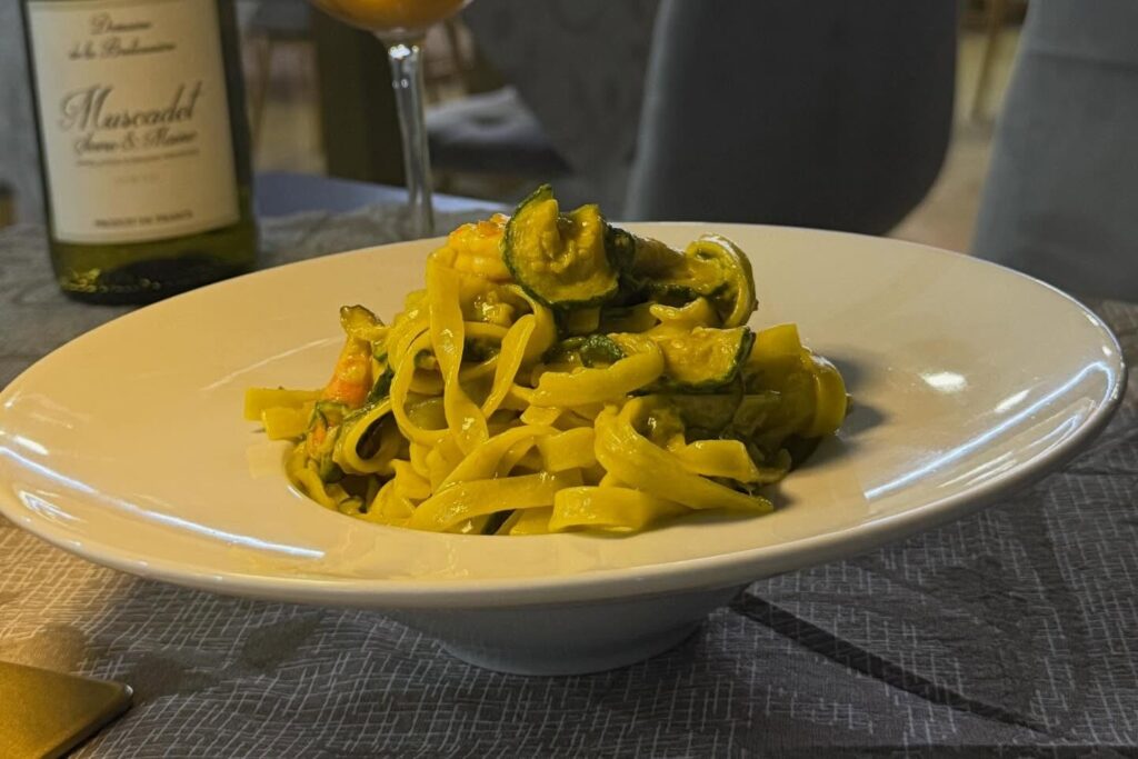 Tagliatelle allo zafferano con zucchine in piatto bianco, sala sullo sfondo